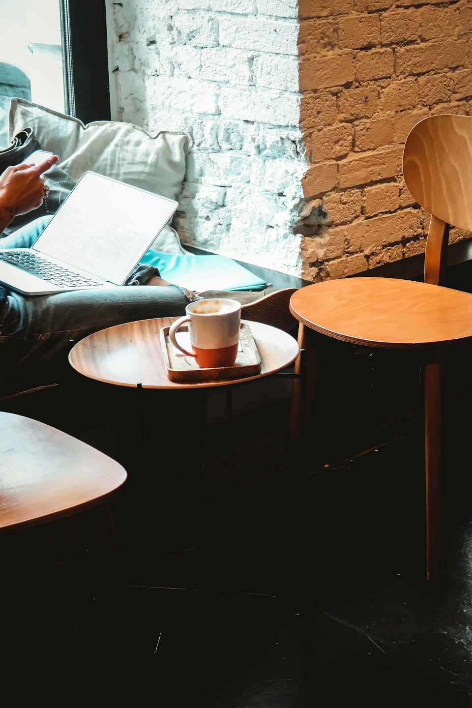 Person working on laptop and phone at cafe table.