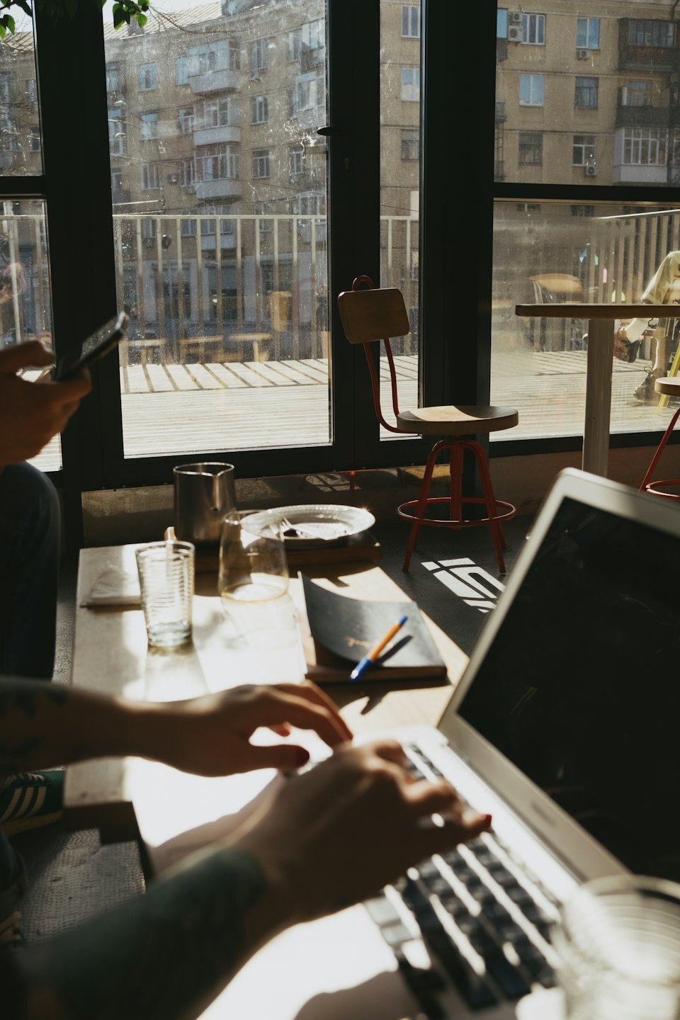 Person typing on a laptop at a sunlit cafe table.