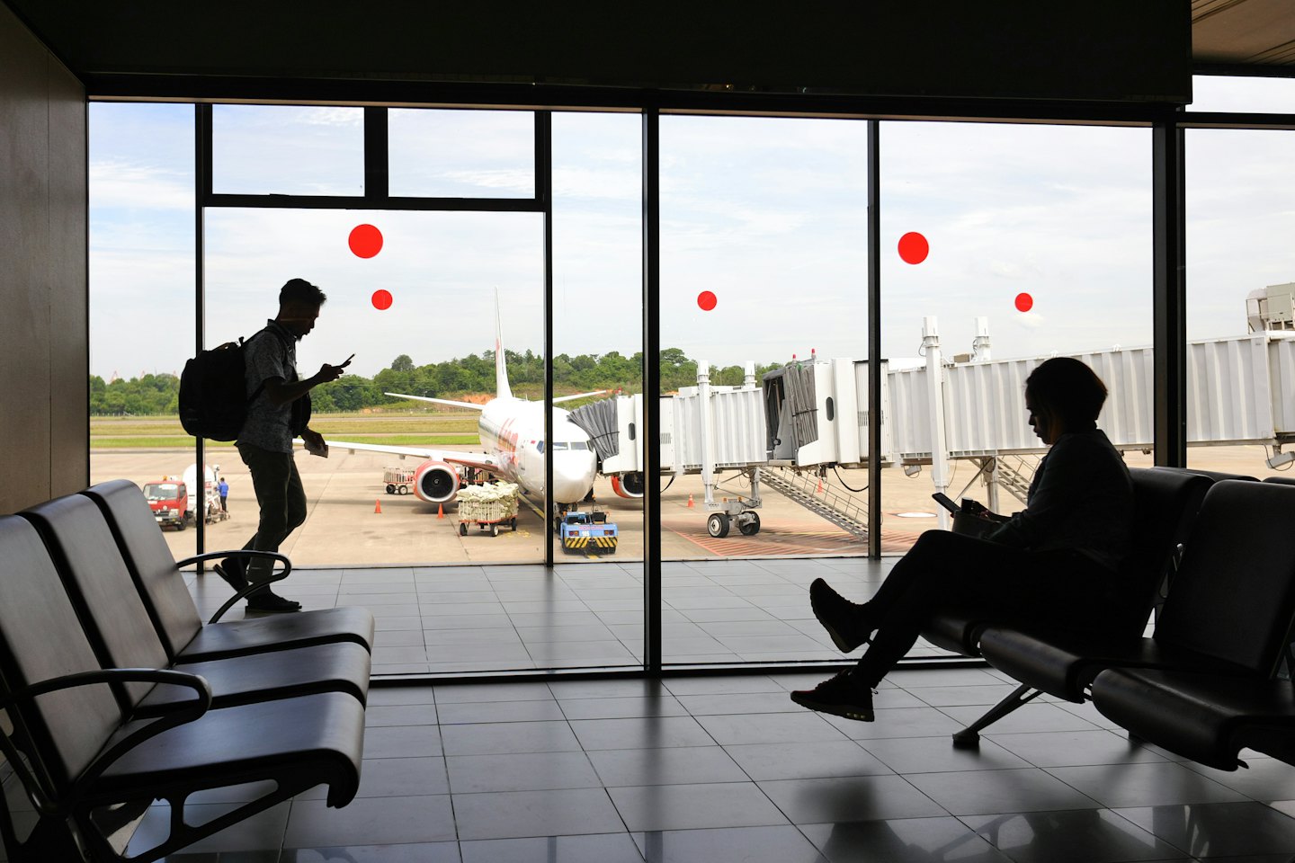 Travelers use phones in airport lounge near airplane.